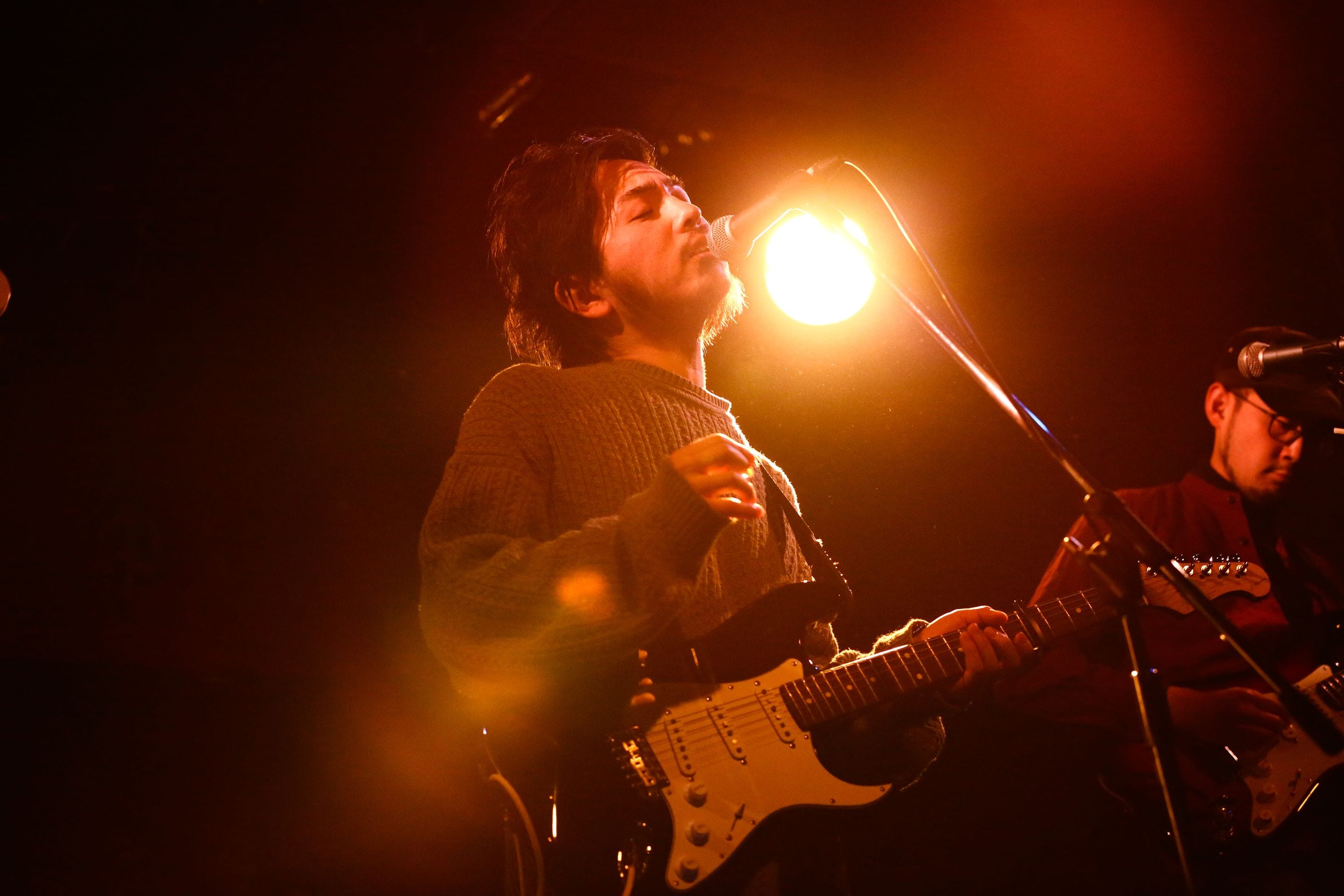 Potomelli singing into the microphone under warm stage light, guitar in hand.